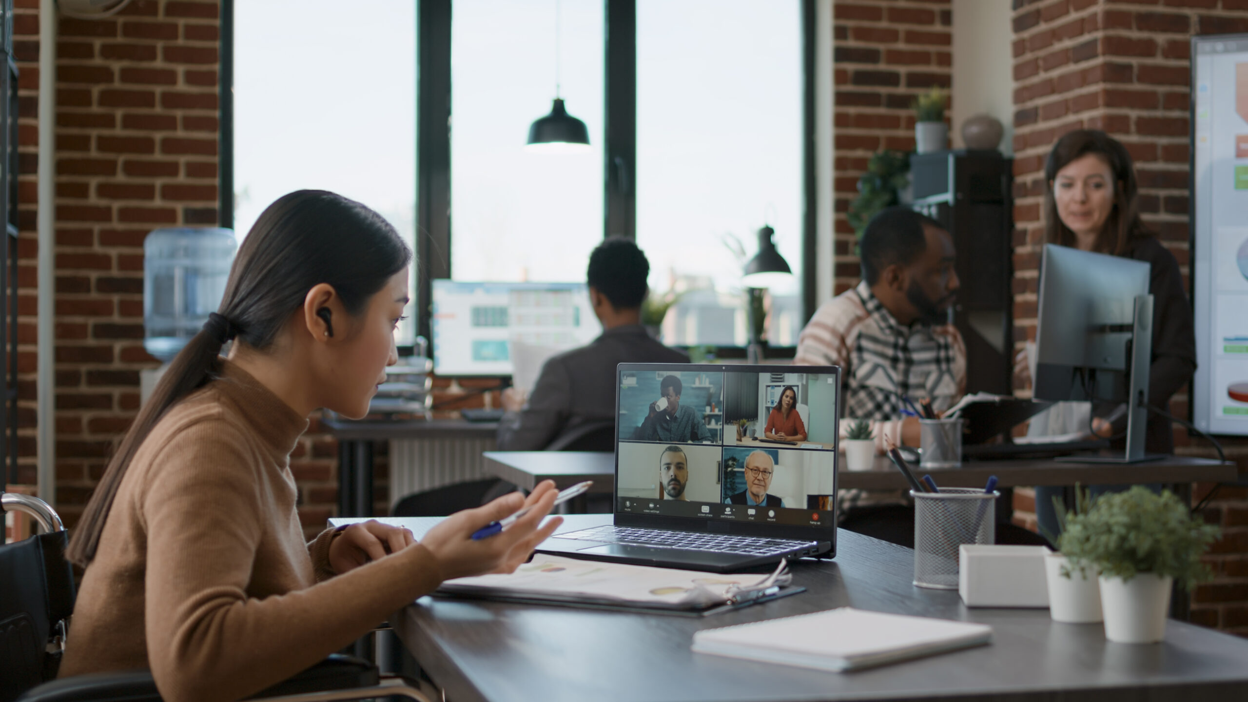Diverse team of people meeting with woman on videocall communication, talking about startup business. Female employee with disability using online videoconference for remote conversation.