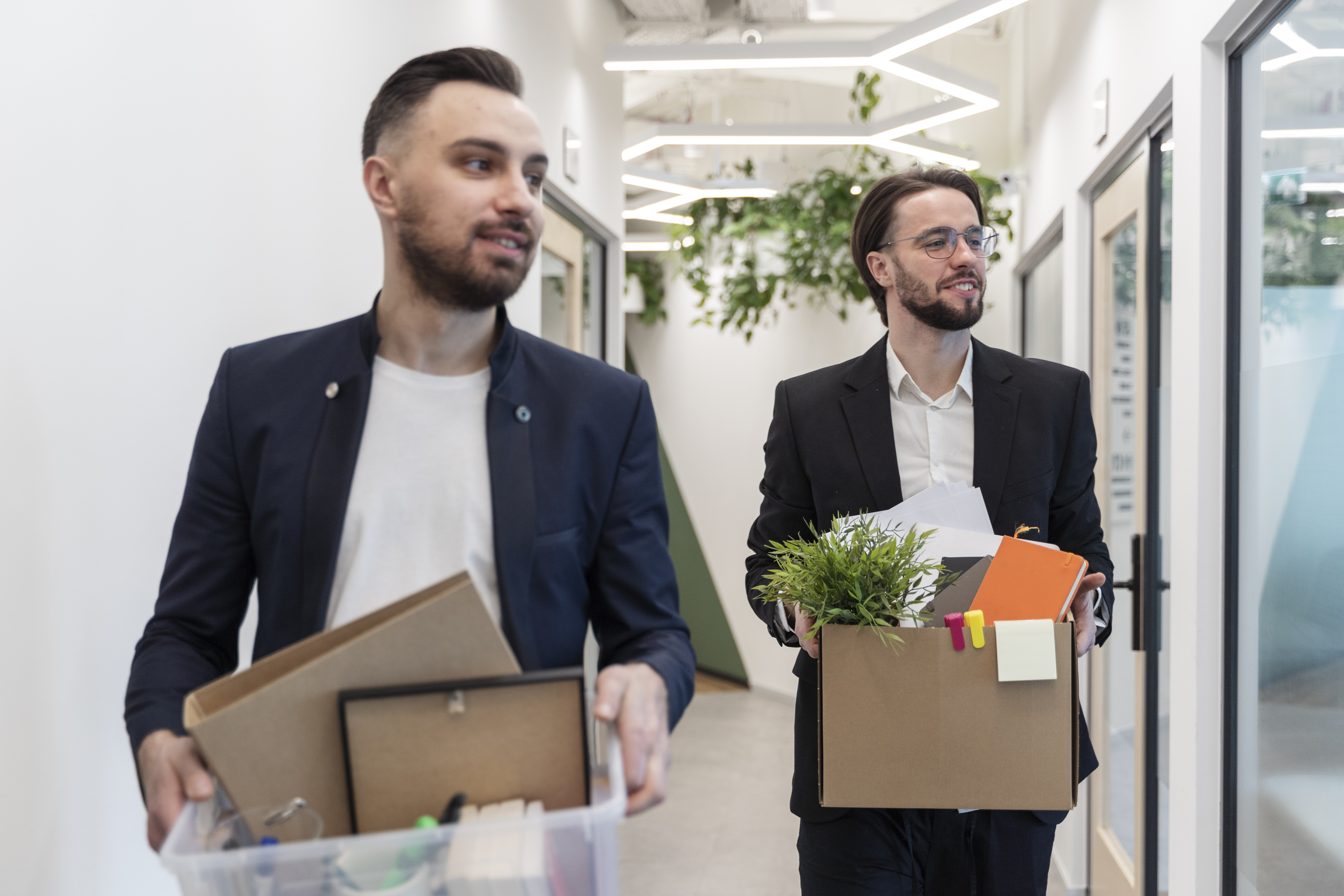 two office workers walking down hallway holding boxes