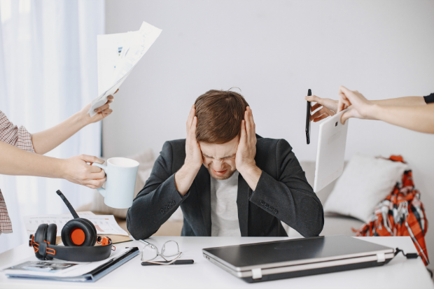 Man sitting on desk overwhelmed with work
