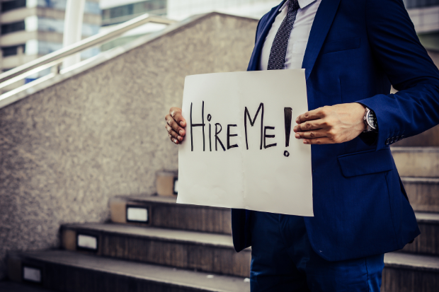 Unemployed man desperately looking for a job holding a need a job sign.