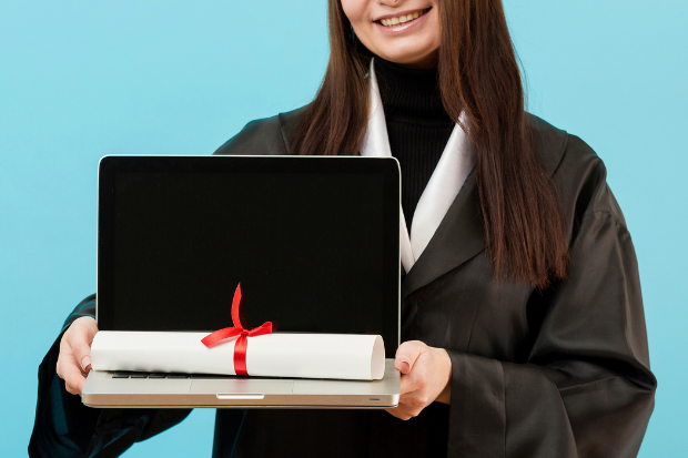 Close-up girl in graduation robes holding laptop